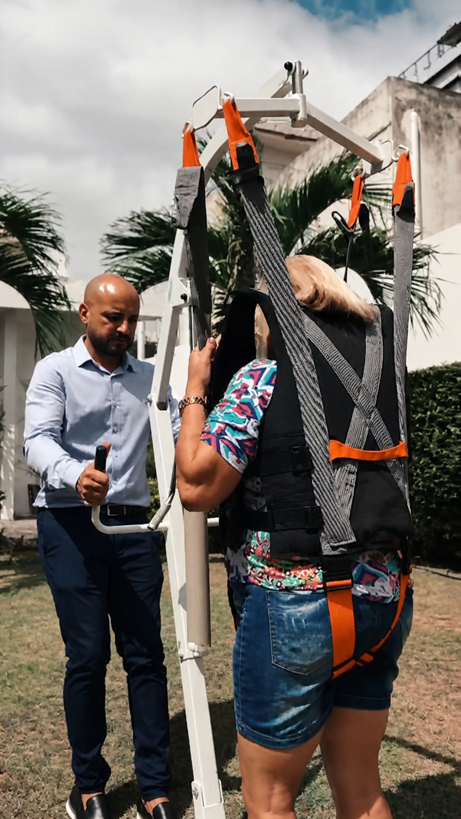 Paciente feminina utilizando guincho de caminhada ao ar livre com auxílio de fisioterapeuta.